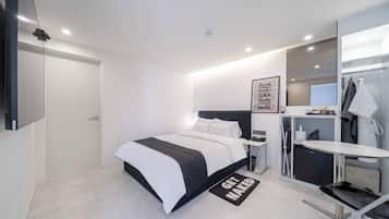 A modern hotel room with a bed, bedside table, and a small desk with a chair.