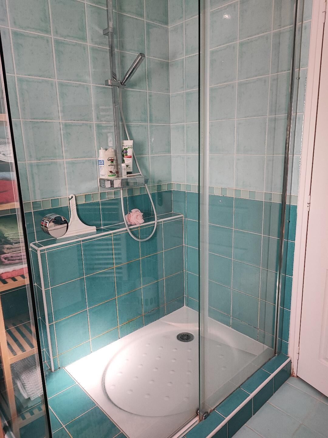 Ducha con paredes de vidrio y suelo blanco, rodeada de azulejos turquesa.