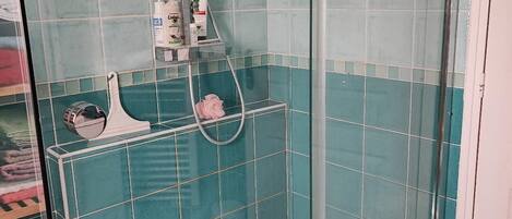 Ducha con paredes de vidrio y suelo blanco, rodeada de azulejos turquesa.