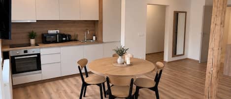 Une cuisine moderne avec des meubles blancs, un plan de travail en bois et une table de salle à manger ronde, accompagnée de quatre chaises.