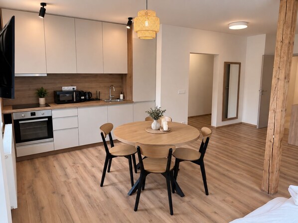 A modern kitchen with white cabinets, a wooden countertop, and a round dining table with four chairs.