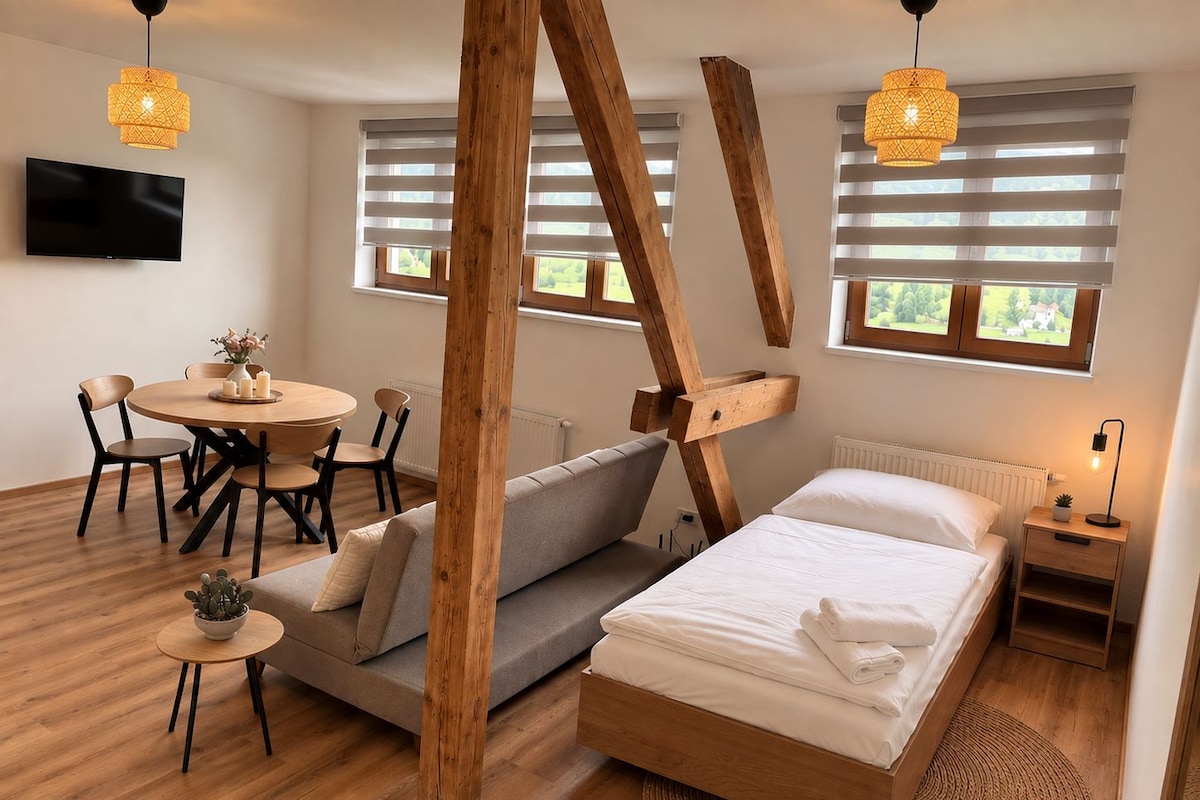 Un dormitorio moderno con una cama de madera, un sofá, una mesa de comedor con sillas y un televisor montado en la pared.