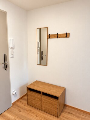 A room with a wooden cabinet, a wall-mounted mirror, a door with a phone and intercom, and a light switch.