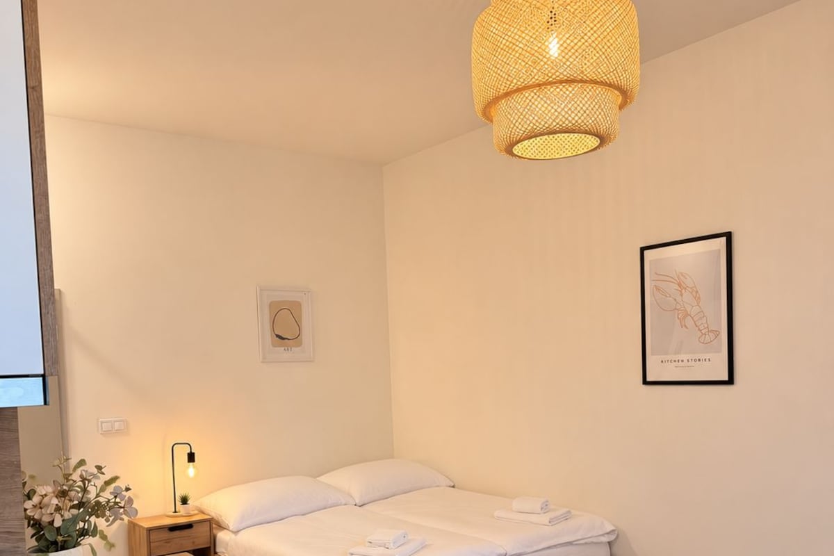 A modern bedroom with a wooden bed, bedside tables, a hanging light fixture, and a framed picture on the wall.