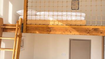 Un dormitorio tipo loft con una escalera de madera, una cama litera, una mesita con una planta y una puerta.
