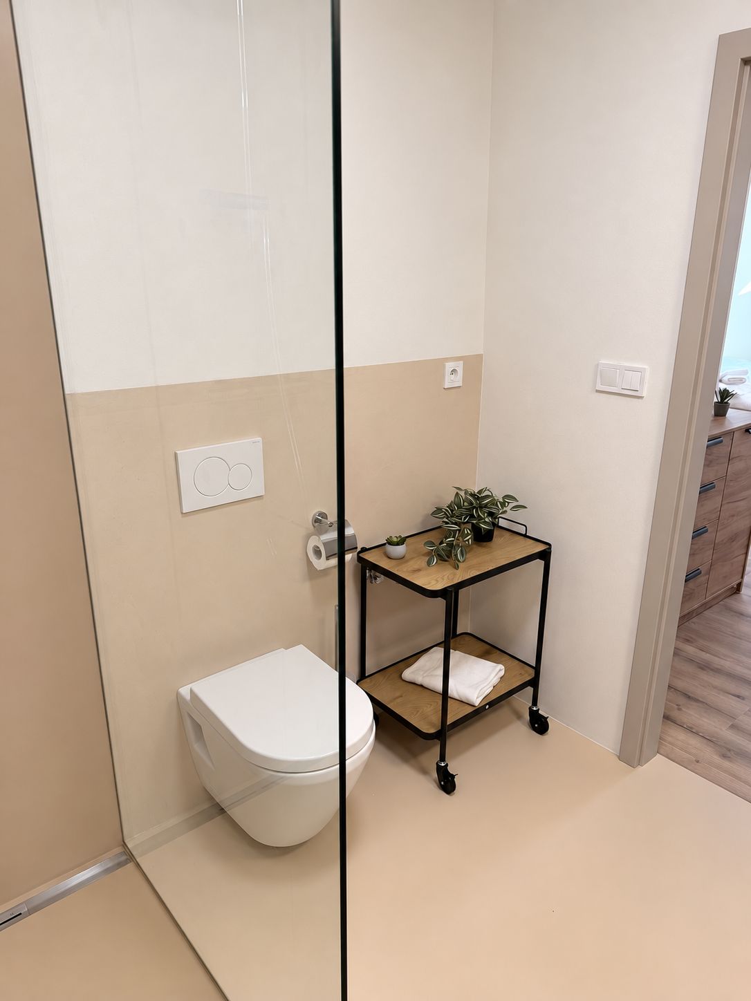 Un baño con inodoro, un pequeño estante de madera con plantas y una zona de ducha.