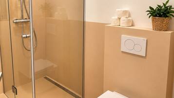 A modern bathroom with a glass-enclosed shower, a white toilet, and a small trash bin.
