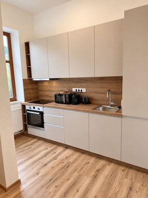 A modern kitchen with white cabinets, a wooden countertop, a built-in oven, a microwave, a toaster, and a sink.