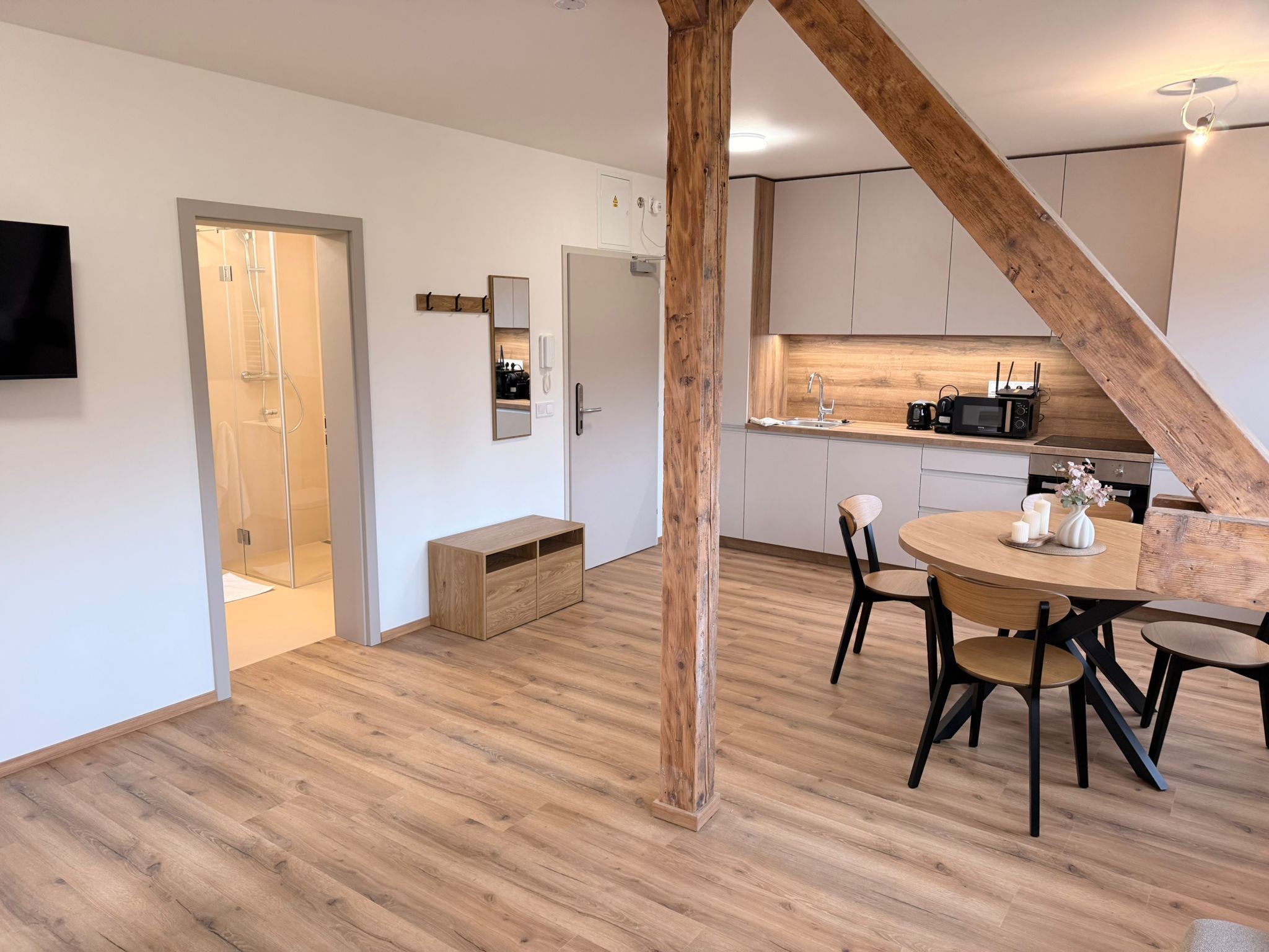 A modern kitchen with wooden flooring, a dining area with a round table, and a visible shower area.