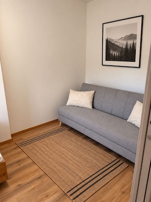 A room with a grey sofa, a woven rug, and a framed picture of a forest on the wall.