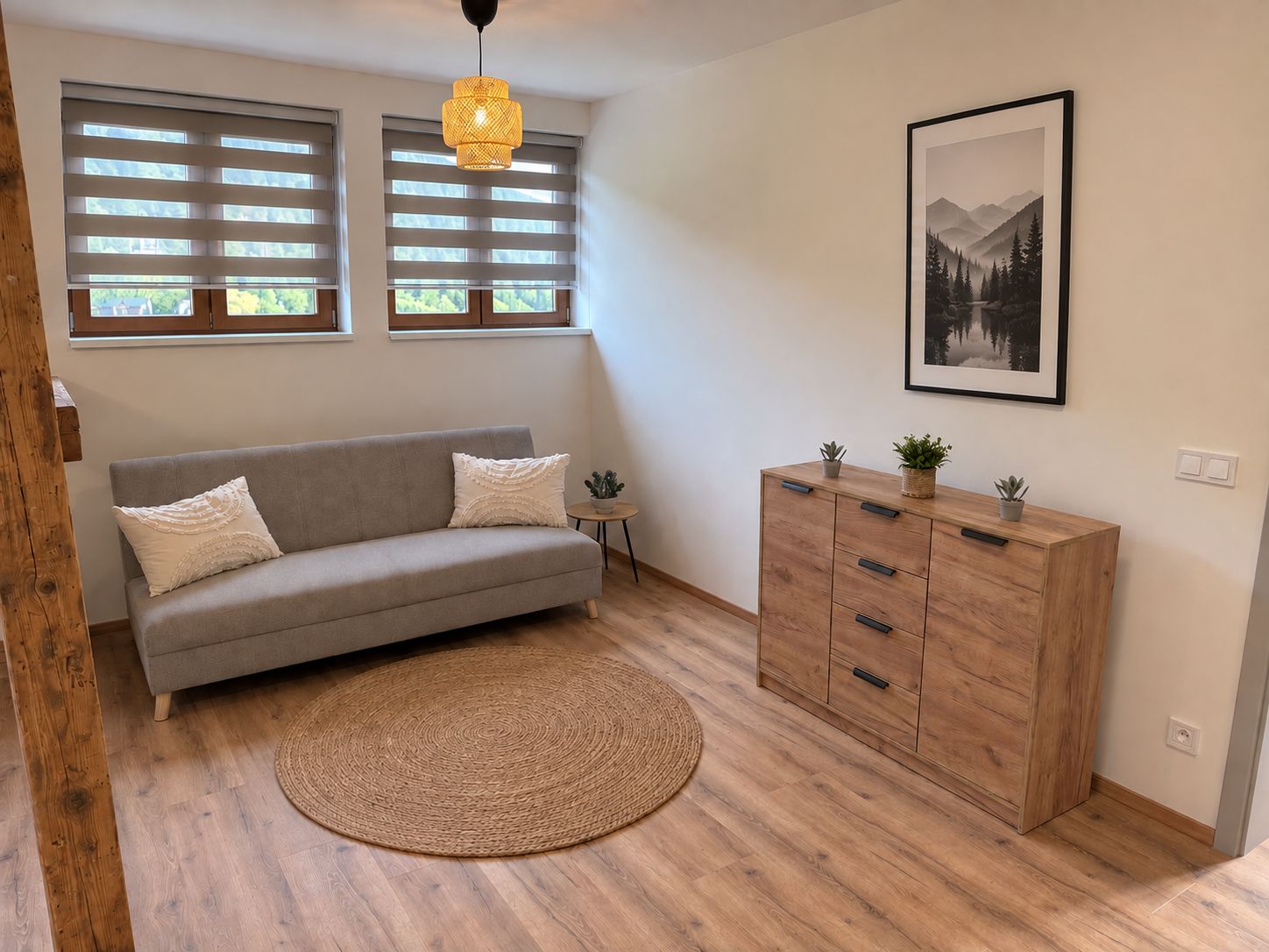 A modern living room with a grey sofa, a wooden cabinet, a woven rug, and a framed picture on the wall.
