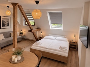 Un dormitorio con una cama grande, un sofá, una mesa de comedor con velas y un televisor montado en la pared.