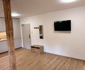 A modern kitchen with wooden flooring, a built-in oven, and a flat-screen TV mounted on the wall.