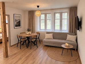 Una sala acogedora con una mesa redonda de madera, un sofá gris y un tapete tejido.