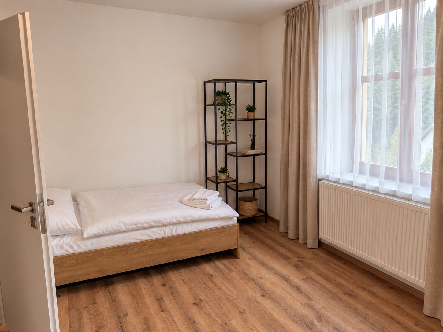 A bedroom with a wooden bed, a window with curtains, a radiator, and a plant shelf.
