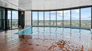 An indoor swimming pool with a view of a cityscape through large windows. - NEW! City Centre One-Bedroom Apartment; Sleeps 4 (Brisbane)