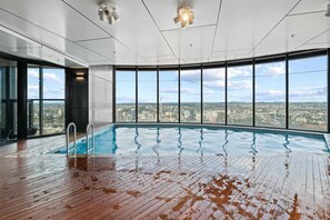 An indoor swimming pool with a view of a cityscape through large windows. - NEW! City Centre One-Bedroom Apartment; Sleeps 4 (Brisbane)