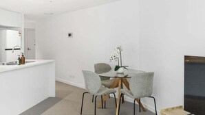 A modern kitchen with a white countertop, a built-in oven, and a sink. There is a dining area with a glass table and four grey chairs. A flat-screen TV is mounted on the wall to the right. - NEW! City Centre One-Bedroom Apartment; Sleeps 4 (Brisbane)