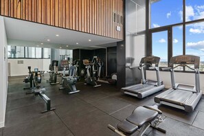Une salle de sport équipée de divers appareils d’exercice, notamment des tapis de course et des appareils de musculation, et dotée de grandes fenêtres offrant une vue sur la ville.