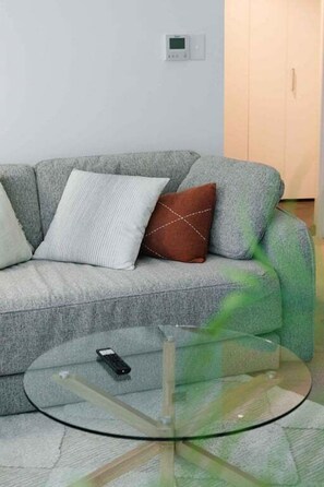 A modern living room with a grey sofa, a glass coffee table, and a remote control on it. - NEW! City Centre One-Bedroom Apartment; Sleeps 4 (Brisbane)