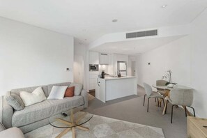 A modern living space with a sofa, a glass coffee table, and a dining area with chairs. - NEW! City Centre One-Bedroom Apartment; Sleeps 4 (Brisbane)