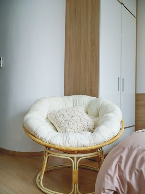 A wicker chair with a cushion and a patterned pillow, positioned in a room with a wooden cabinet and a white wardrobe. -  Babo Homestay 1 Da Nang (Da Nang)