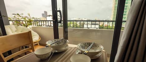 Un coin repas avec une table dressée pour quatre personnes, une chaise et une vue sur le paysage urbain, visible à travers une porte vitrée.
