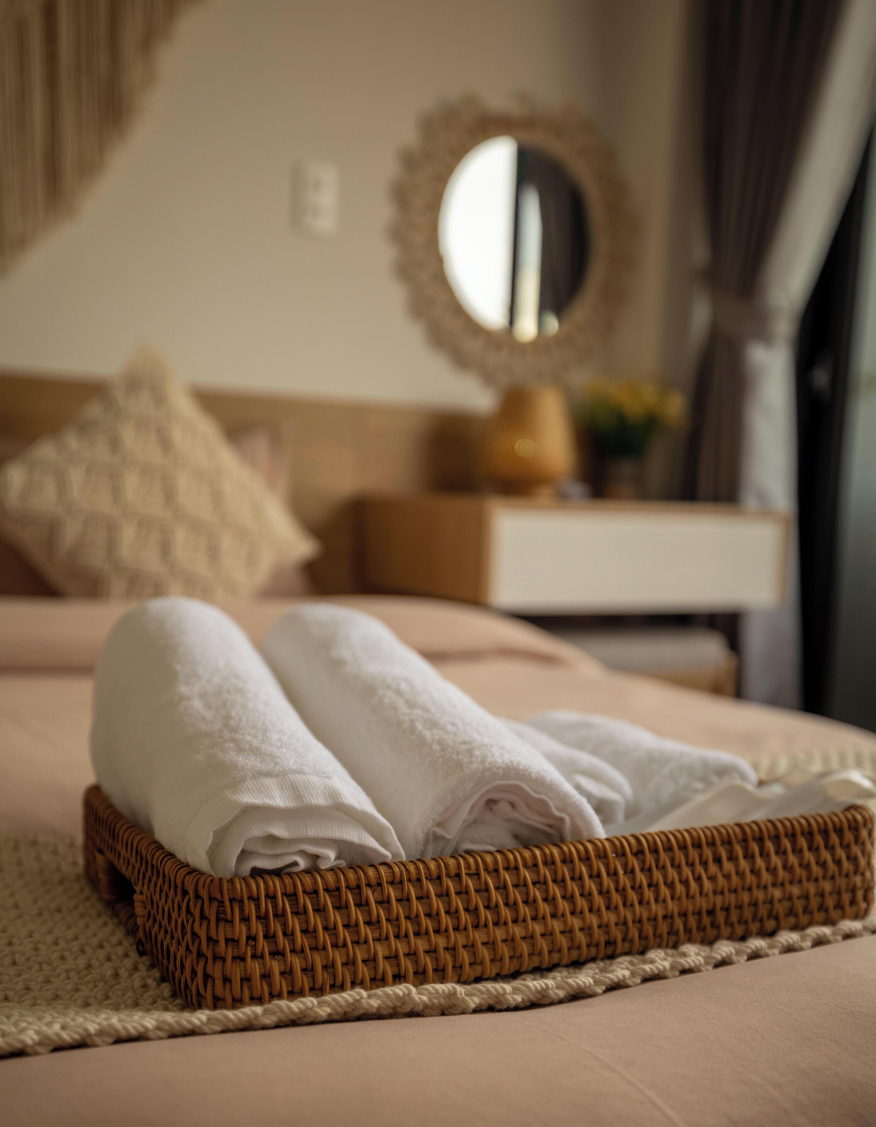 A neatly made bed with a folded white towel, a wicker tray, and a woven rug.