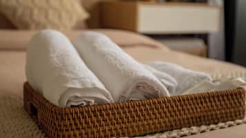 A neatly made bed with a folded white towel, a wicker tray, and a woven rug.
