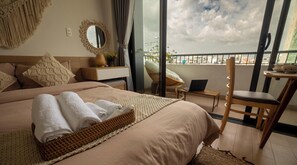 Ein Hotelzimmer mit einem Bett, einem Laptop auf einem kleinen Tisch, einem Sessel und einem Balkon mit Blick.