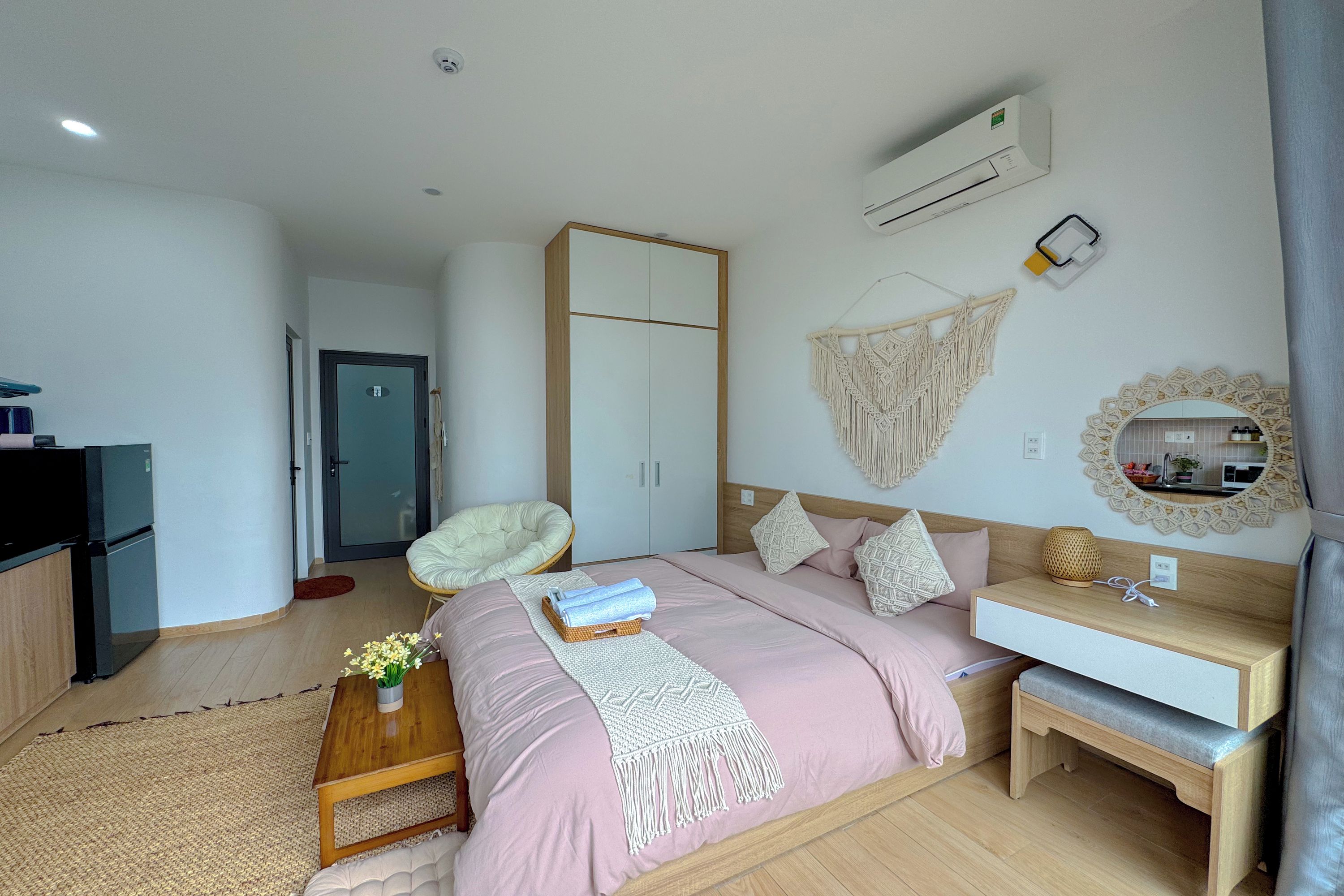 A bedroom with a bed, bedside table, chair, wardrobe, and an air conditioning unit.