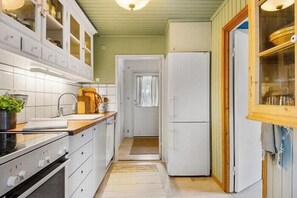 A narrow kitchen with white cabinets, a stove, and a refrigerator. - Authentic Swedish summer house at Asnæs plantation (Asnæs)