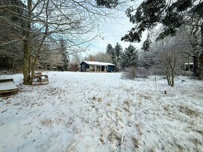 Schneebedeckte Landschaft mit einem Haus, einer Bank und einem Baum.