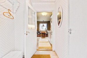 Ein Flur, der in einen Essbereich führt, mit einem Tisch, Stühlen, einem Spiegel an der Wand und einem strukturierten Wanddesign.