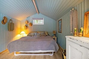 Un dormitorio con cama, mesita de noche, lámpara y sombreros colgados en la pared.
