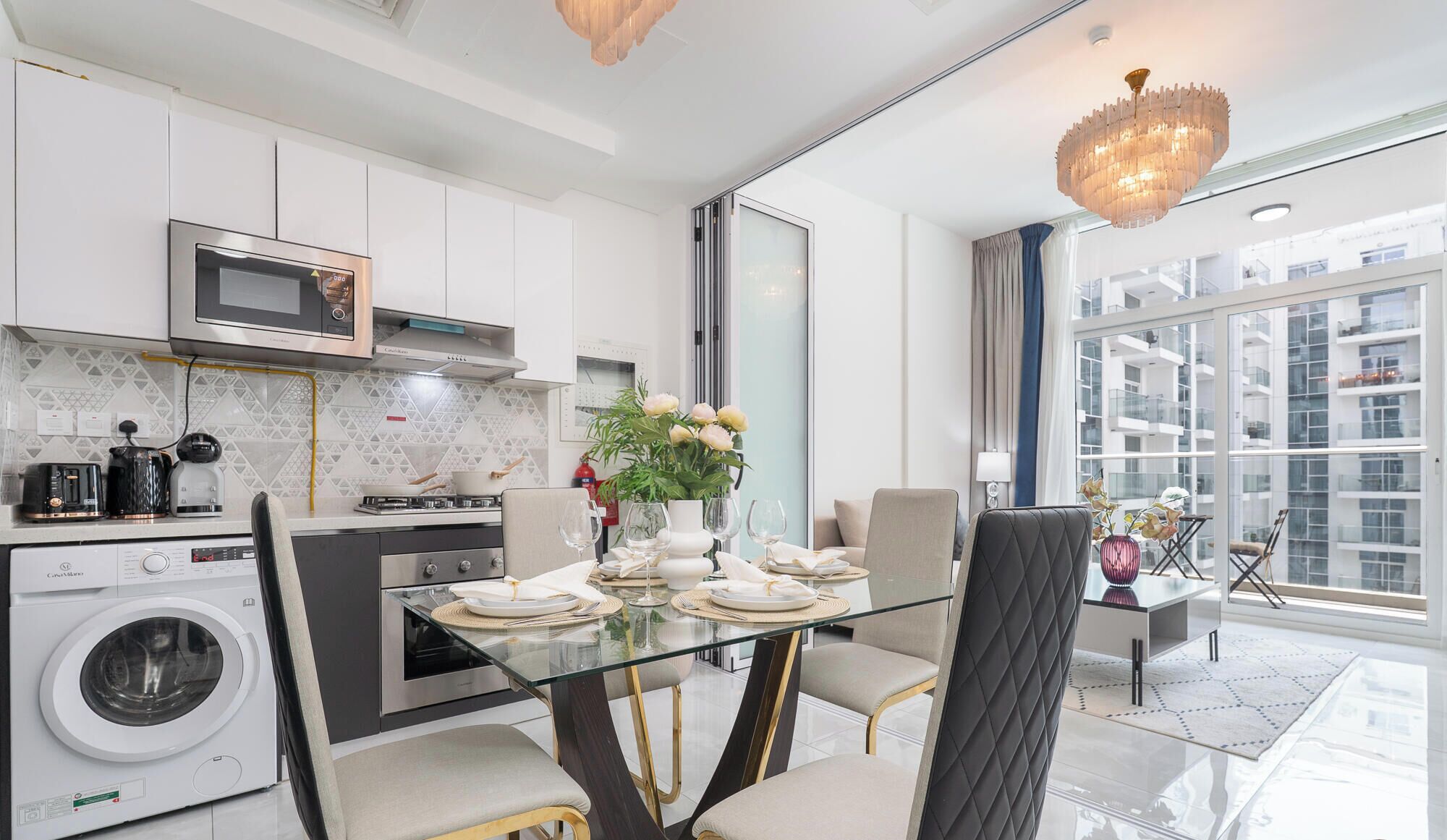 A modern kitchen with a glass dining table, stainless steel appliances, and a view of the city through large windows.