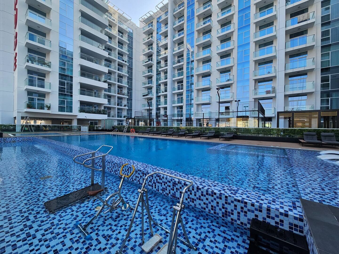 A modern hotel with a swimming pool, multiple balconies, and a contemporary architectural design.