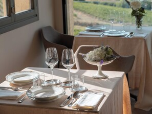 A dining table set with plates, glasses, and cutlery, with a floral centerpiece and a view of the outdoors.