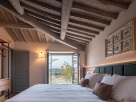 Una camera da letto con un letto grande, soffitto in legno, vista attraverso una porta aperta e opere d'arte appese alle pareti.