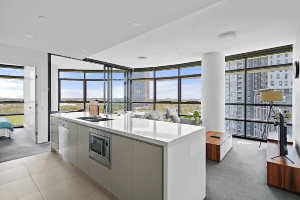 A modern kitchen with a central island, large windows, and a view of the cityscape. - Park View 2BR With Secure Parking | Near to Mall (Sydney Olympic Park)