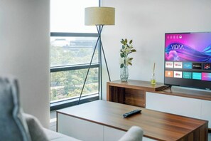 Een moderne woonkamer met een flatscreen televisie waarop verschillende streamingdiensten worden getoond, een houten salontafel, een afstandsbediening, een vaas met bloemen en een vloerlamp.