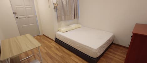 Un dormitorio con cama, piso de madera, puerta blanca y un armario rojo.