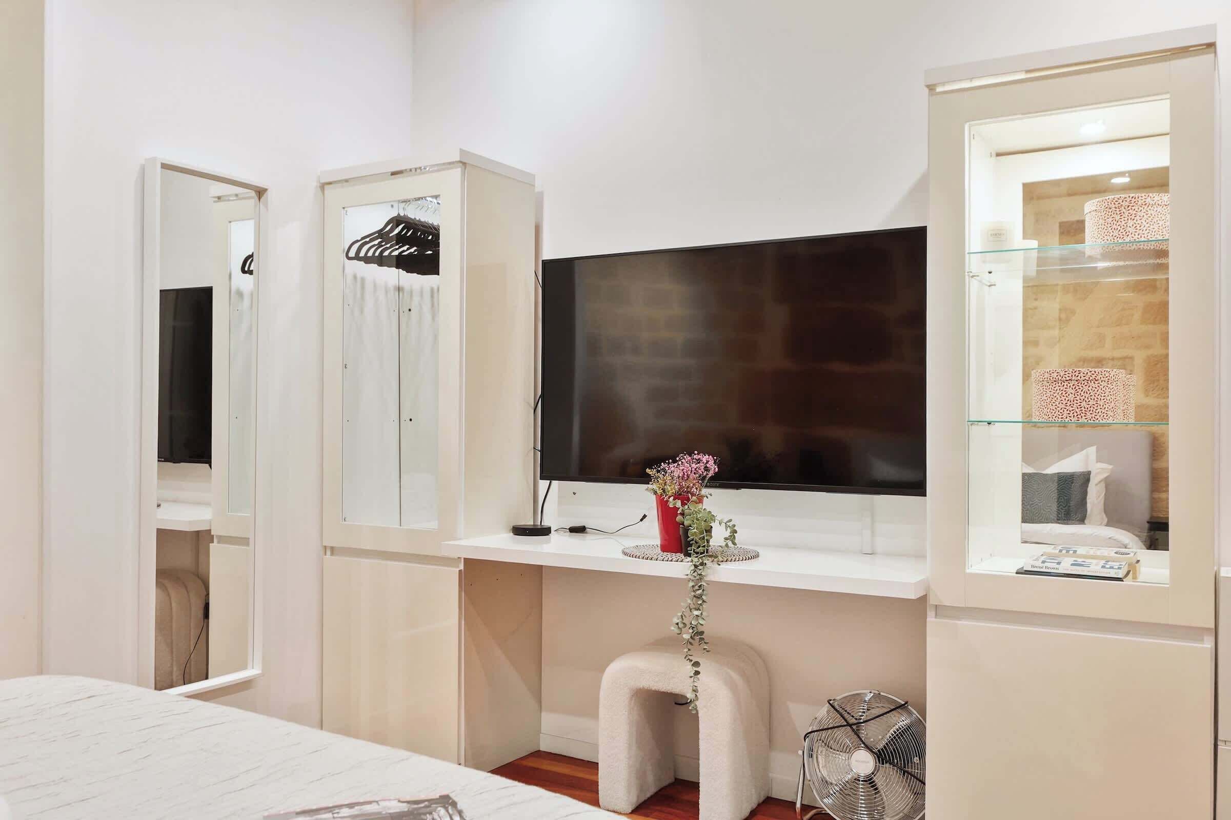 Un dormitorio con cama, escritorio con ordenador, televisor y armario.