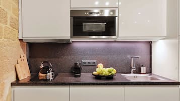 Una cocina con horno de acero inoxidable, hervidor, frutero y lavaplatos.