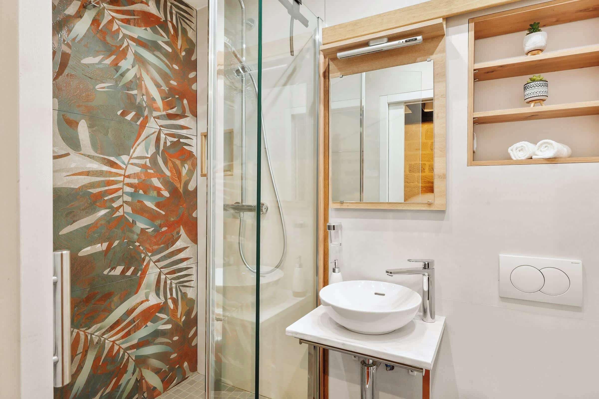 A bathroom with a glass shower enclosure, a white sink, and a mirror above it.