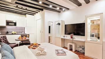 Una habitación de hotel con cama, escritorio con televisor, kitchenette y baño.