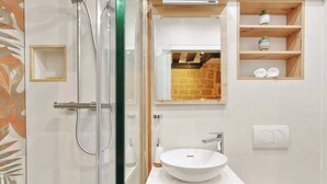 Ein Badezimmer mit Duschkabine aus Glas, einem weißen Waschbecken und einem Spiegel darüber.