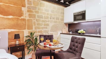 Una habitación acogedora con pared de piedra, una cama, una pequeña mesa con desayuno y una kitchenette.