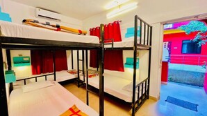 A hostel room with bunk beds, a desk with a chair, and a window with red curtains. - Mitra Hostel (Arambol)