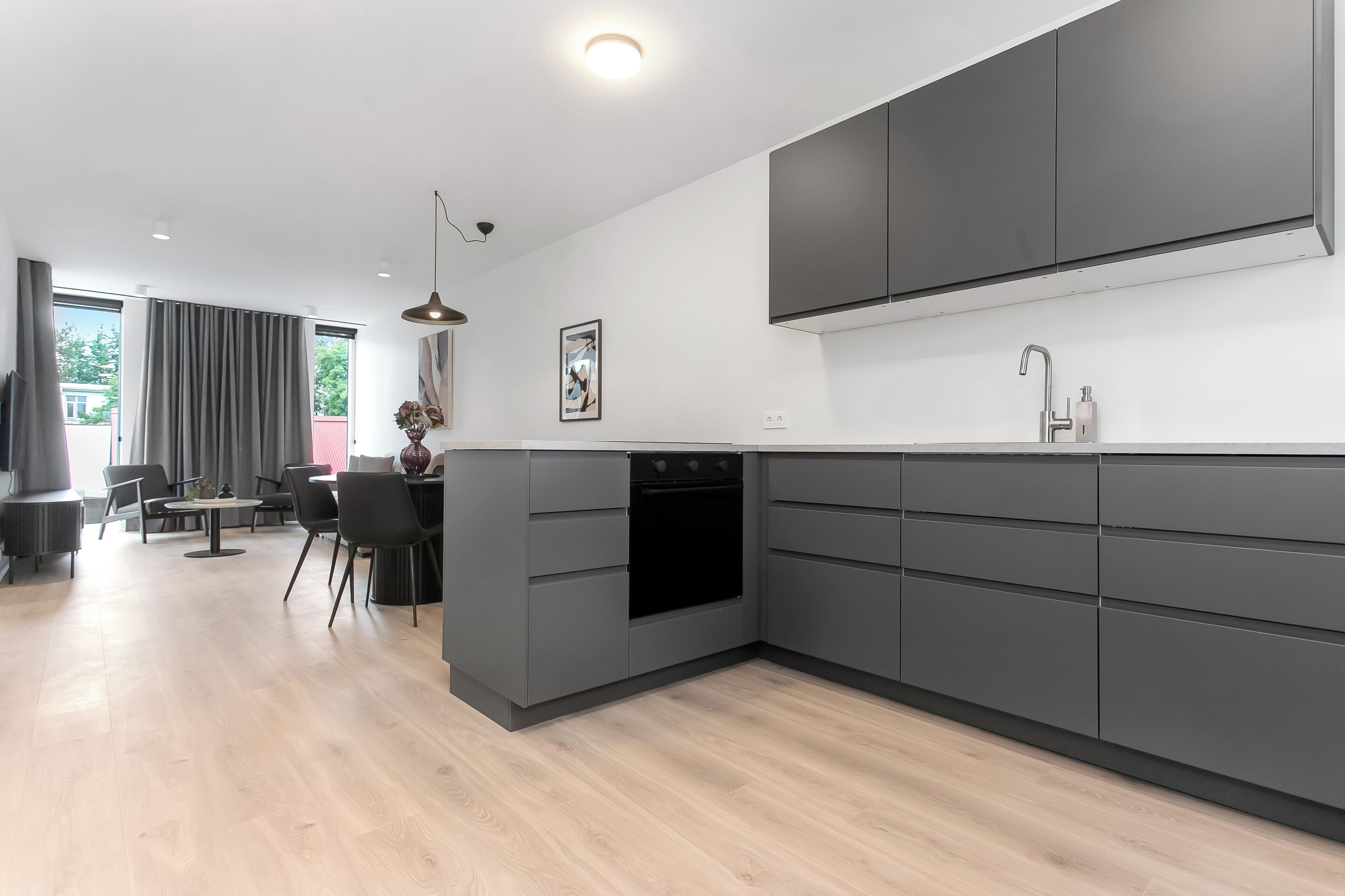 Una cocina moderna con armarios grises, un horno empotrado y una zona de comedor con mesa y sillas.